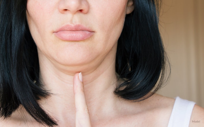Woman pointing to her double chin that could be reduced with KYBELLA®.
