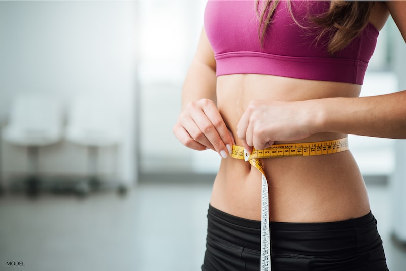 Thin woman wrapping a tape measure around waist to show weight loss.