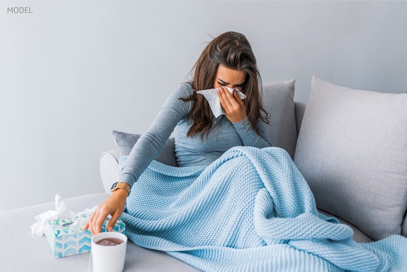 Woman on the couch with blankets and tissues.