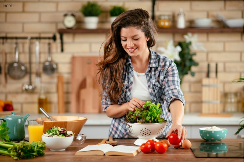 oung women preparing a vegetable salad in the kitchen.